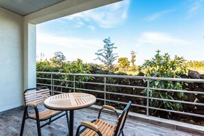 Ein Balkon mit rundem Tisch und zwei Stühlen, der auf einen Garten mit verschiedenen Pflanzen und einer Steinmauer blickt.