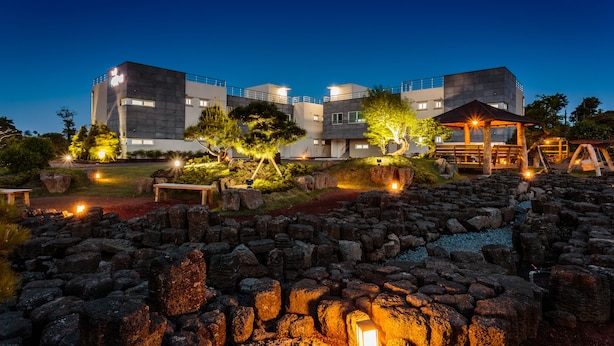 Un edificio moderno con varios pisos, mobiliario exterior y un jardín bien iluminado al anochecer.