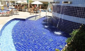 A swimming pool with a blue mosaic tile design, surrounded by lounge chairs and umbrellas.