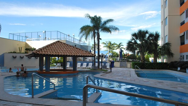 Un área de piscina con un pabellón, palmeras y un edificio con balcones.
