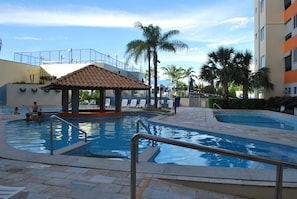 Un espace piscine agrémenté d’un kiosque, de palmiers et d’un bâtiment doté de balcons.