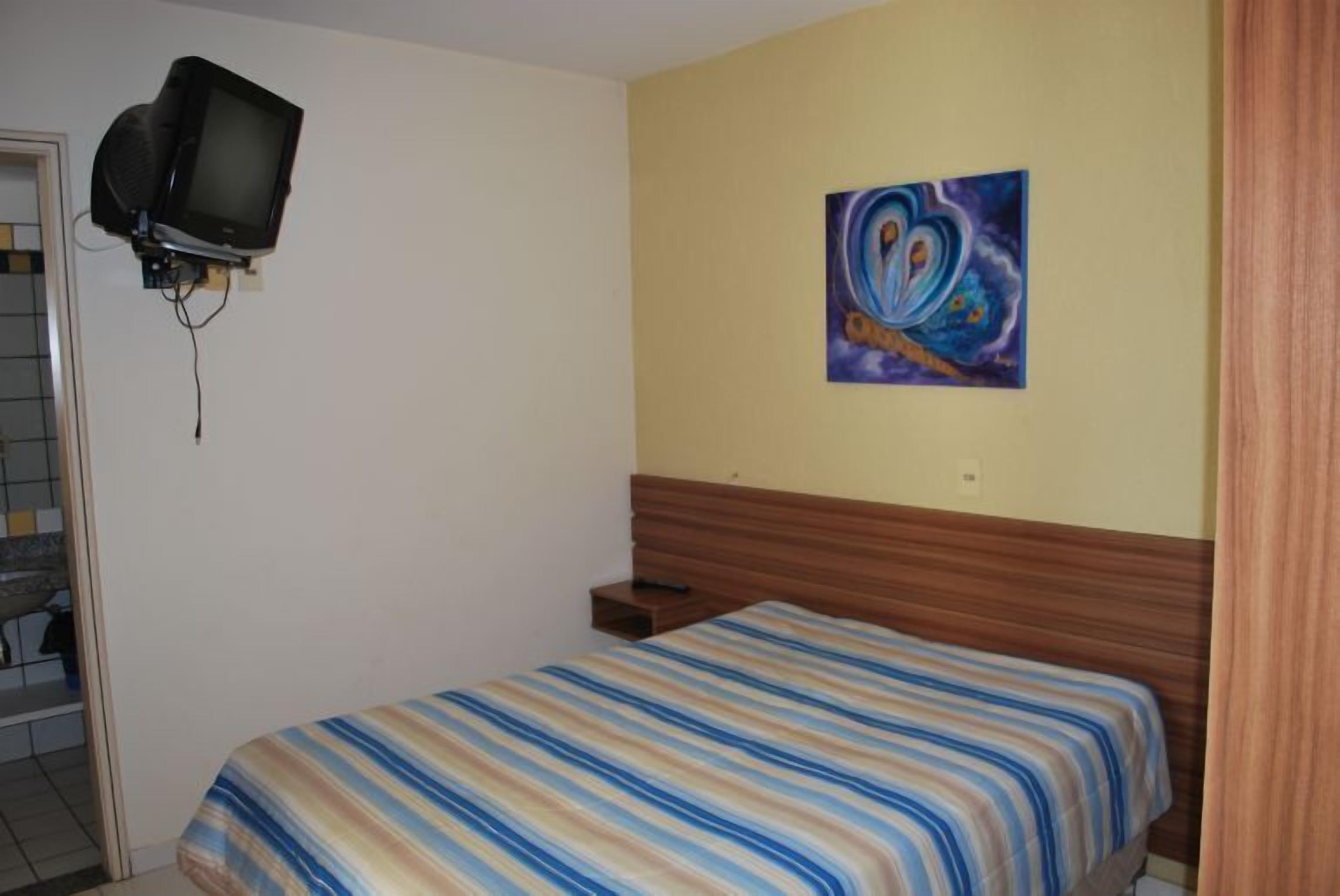 Ein Schlafzimmer mit einem Bett, einem an der Wand montierten Fernseher und einem Bild über dem Bett.