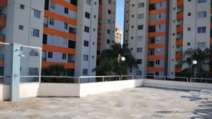 Un edificio residencial de varios pisos con balcones, un patio empedrado y palmeras.