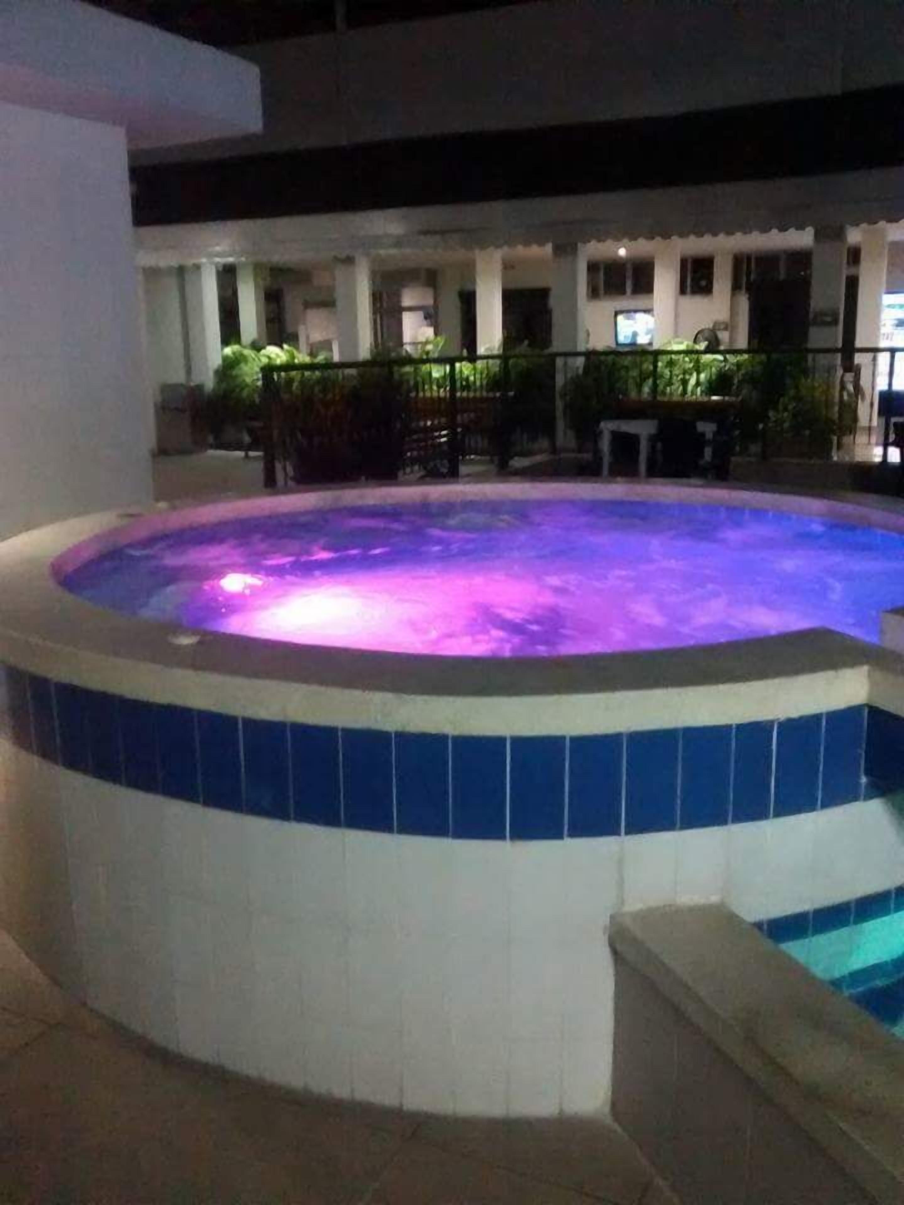 A hot tub with a tiled edge and a pool in the background.