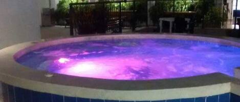 A hot tub with a tiled edge and a pool in the background.