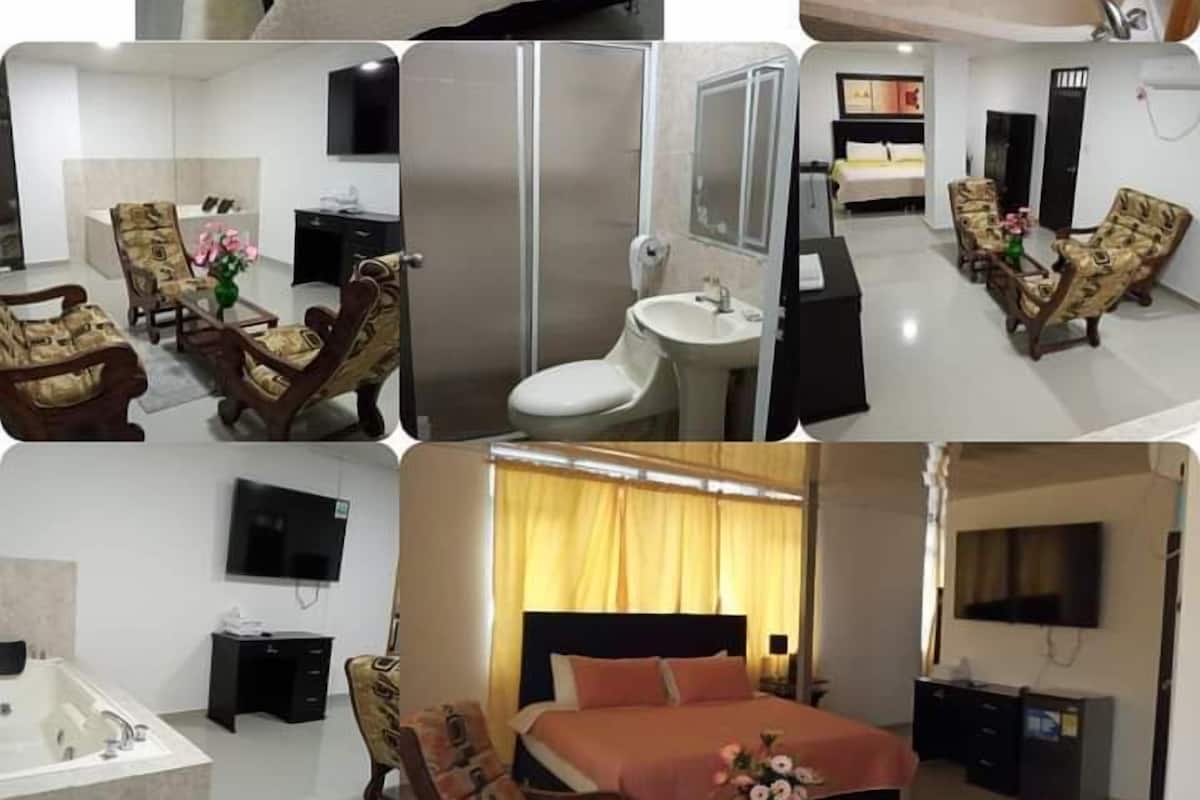 A hotel room with a bed, a bathroom with a bathtub, a sitting area with chairs, a TV, and a desk.
