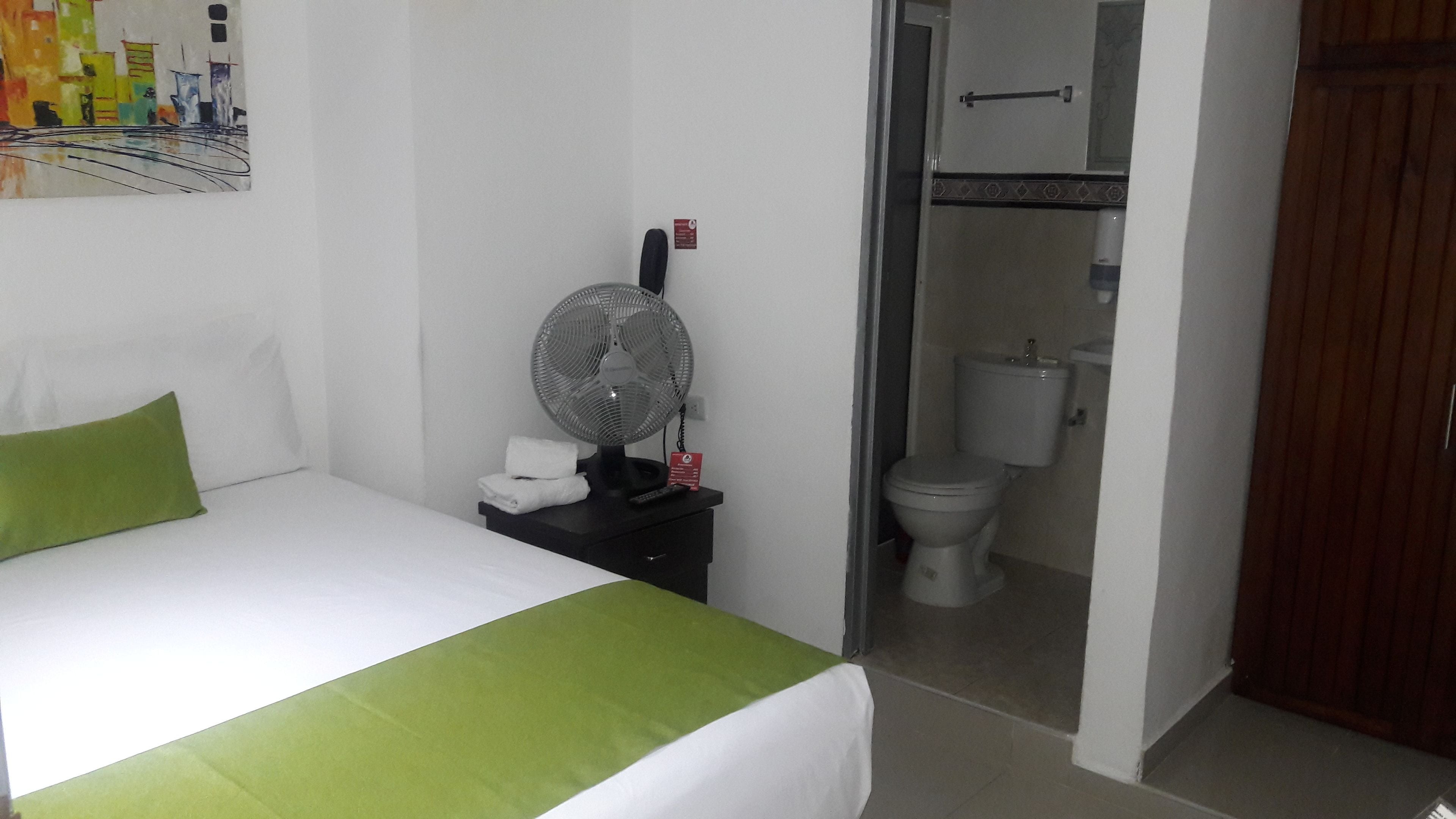 Ein Hotelzimmer mit einem Bett, einem Nachttisch mit Ventilator und Blick ins Badezimmer.
