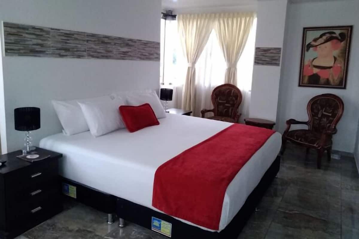 A hotel room with a large bed, a nightstand with a lamp, a chair, and a painting on the wall.