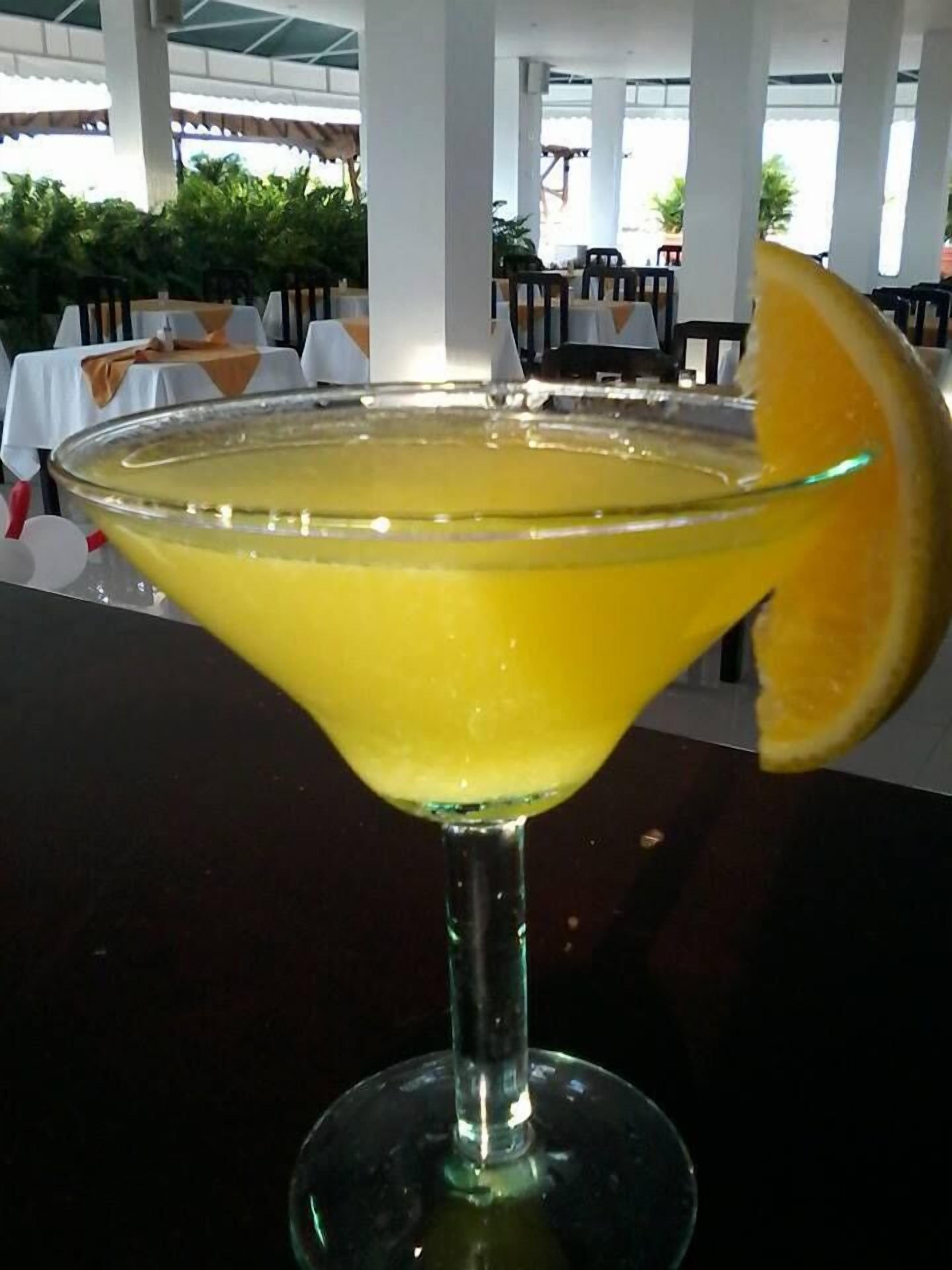 A cocktail in a martini glass with a slice of orange on the rim.