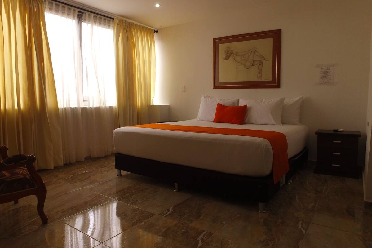 A hotel room with a bed, a nightstand, a chair, and a painting on the wall.