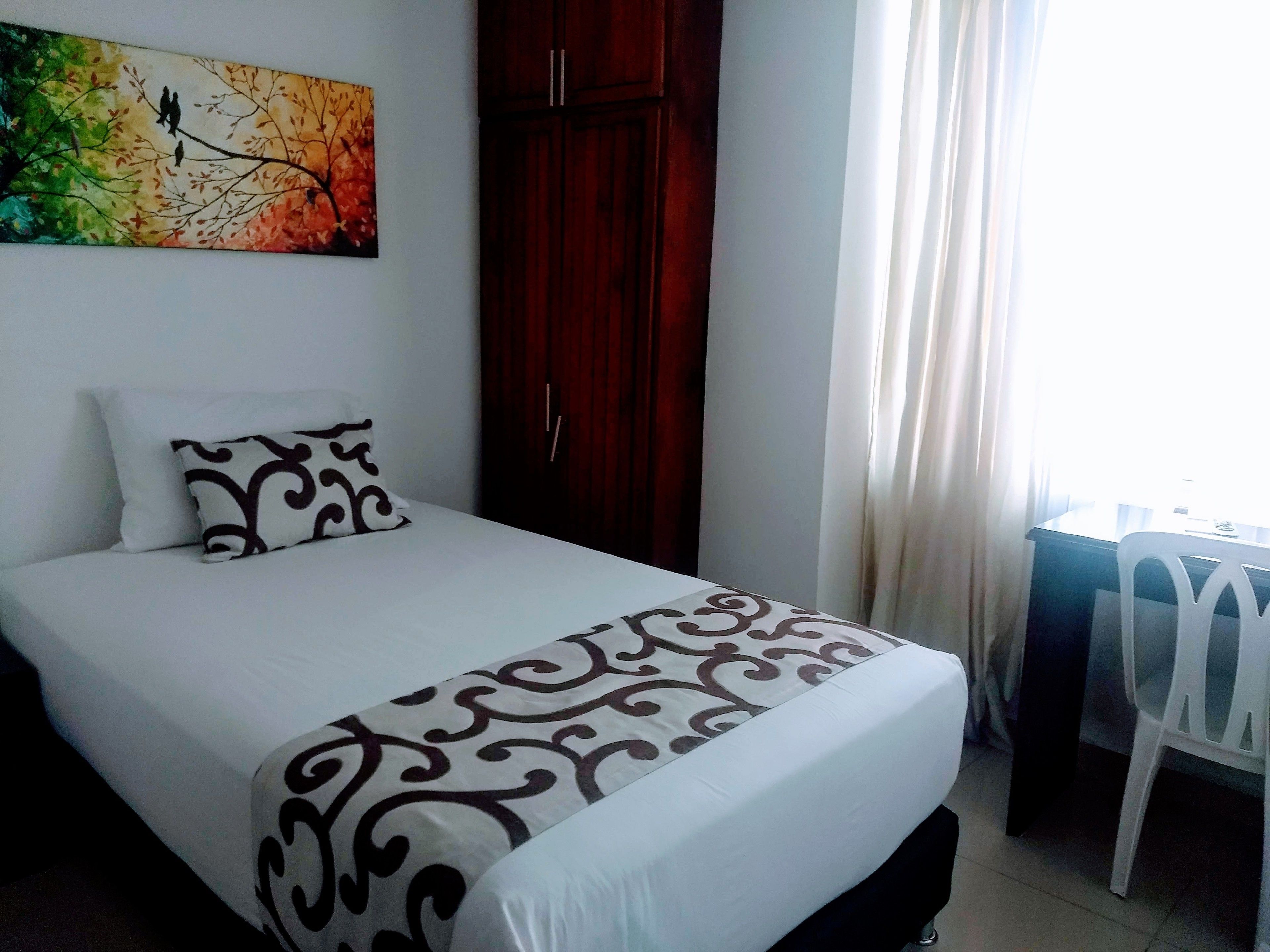 A neatly made bed with patterned bedding, a wooden wardrobe, and a window with curtains.
