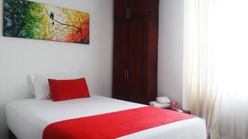 Habitación de hotel con cama, almohada roja, colcha blanca, manta roja, un cuadro en la pared, armario, mesita de noche con teléfono y cortina.