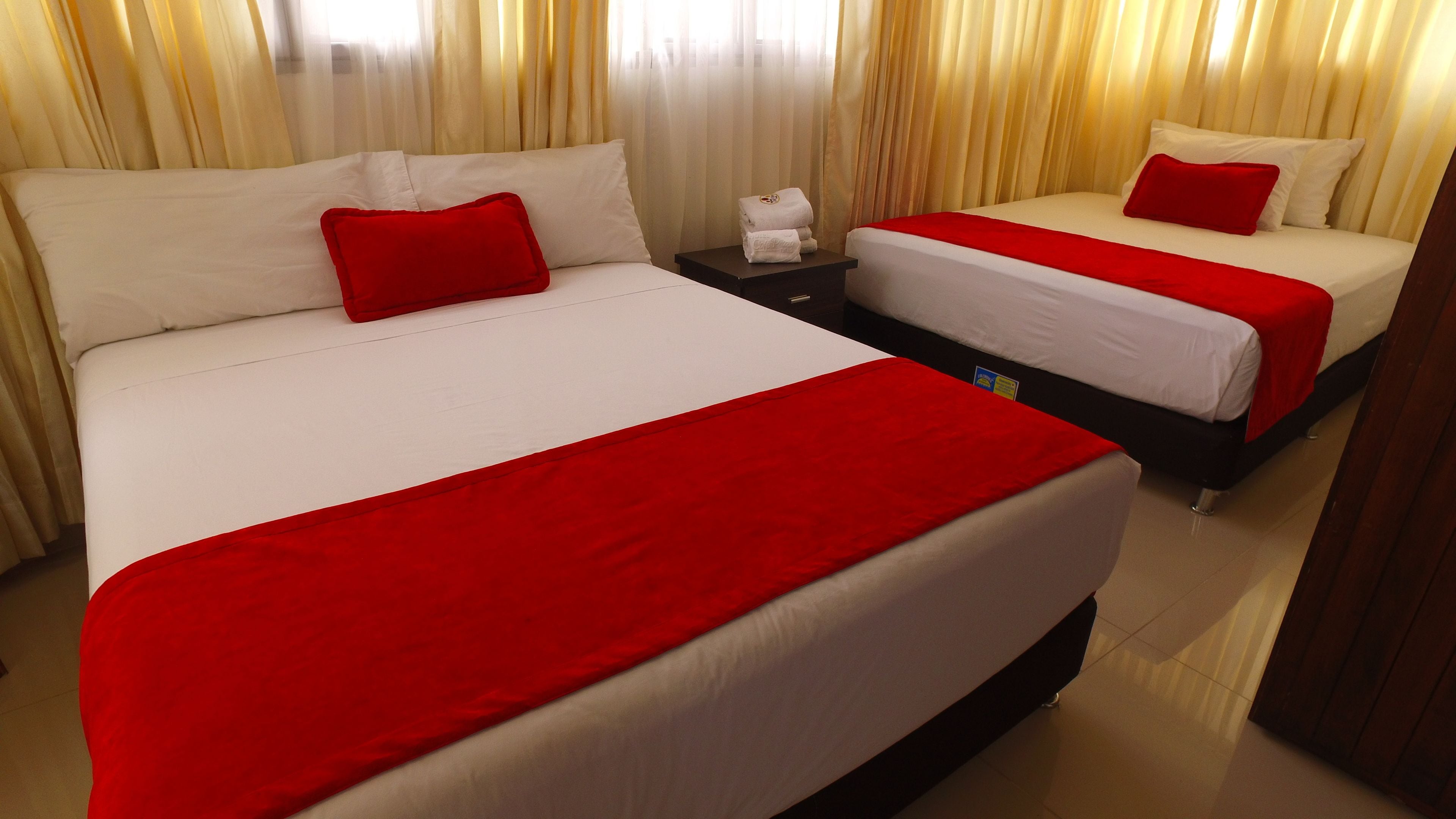 A hotel room with two beds, each with white bedding and red accents.