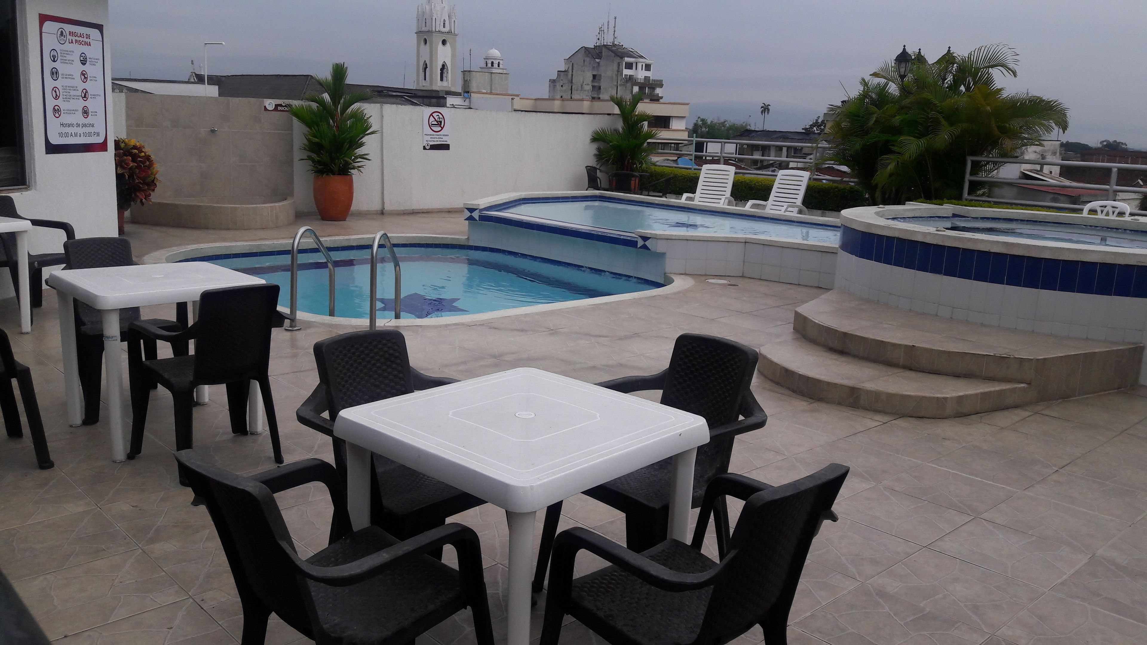 A rooftop pool area with multiple pools, lounge chairs, and tables.