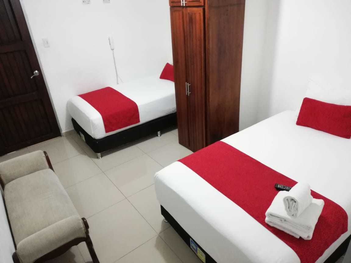 A hotel room with two single beds, a wooden wardrobe, a chair, and a red and white bedspread.