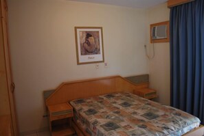 Ein Schlafzimmer mit einem hölzernen Bett, einem Nachttisch, einer wandmontierten Klimaanlage und einem gerahmten Bild an der Wand.
