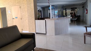 A modern lobby with a reception desk, a sofa, and a glass partition. - Thermas das Caldas - Achei Férias (Caldas Novas)