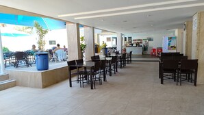 A spacious indoor area with multiple tables and chairs, a counter with a refrigerator, and a view of the outside. - Thermas das Caldas - Achei Férias (Caldas Novas)