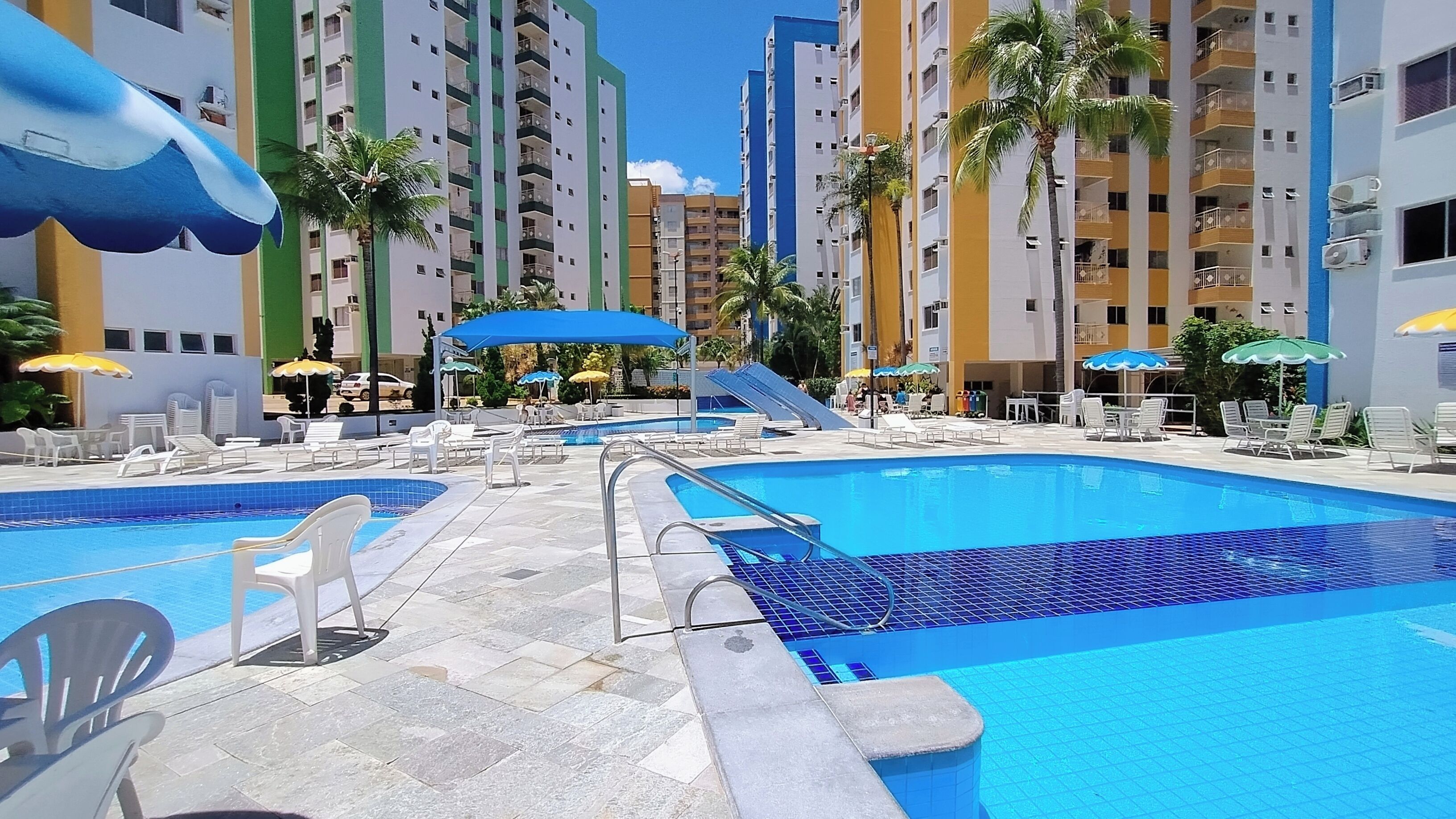 Área de piscina em resort, com várias piscinas, espreguiçadeiras e guarda-sóis.