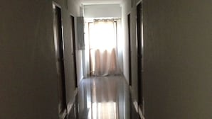 Un pasillo largo y estrecho con piso reflectante que lleva a una habitación luminosa con ventana y cortinas.