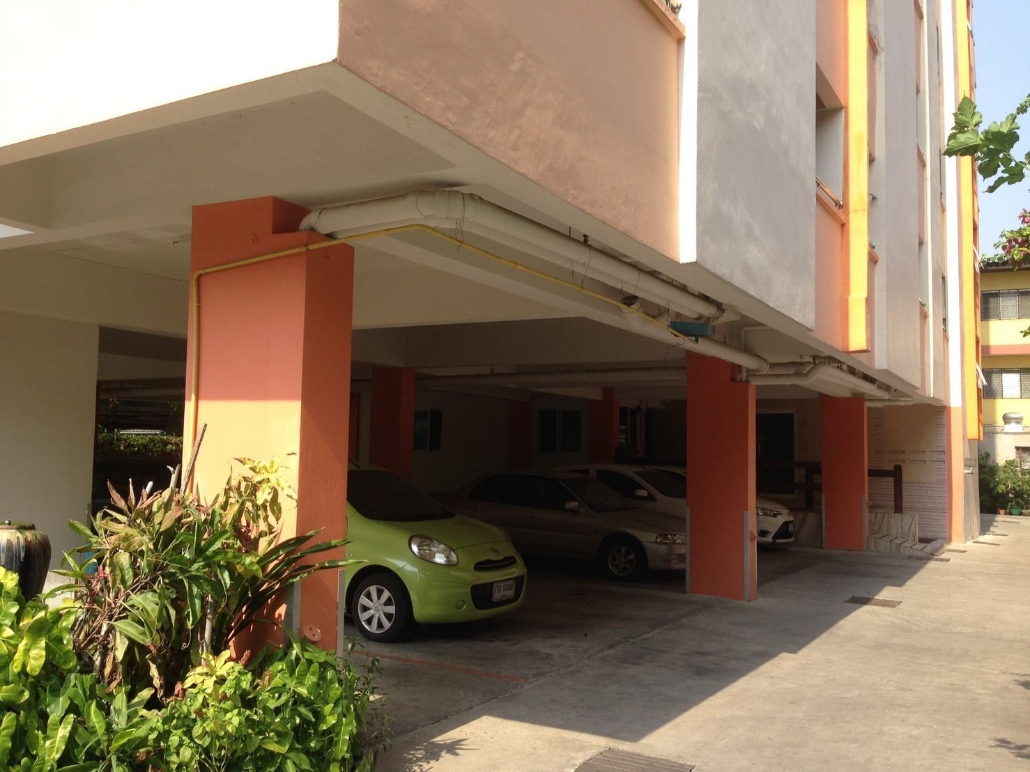 Un estacionamiento con dos autos estacionados bajo un edificio con pilares naranjas.