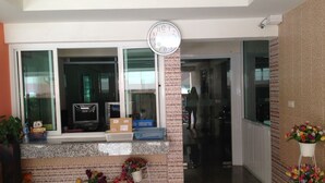 Zona de recepción con un reloj, una ventana con un letrero de bienvenida y un mostrador con cajas y una cesta.