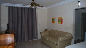 Una sala de estar con un sofá color beige, un aparador de madera, un ventilador de techo y dos obras de arte en las paredes.