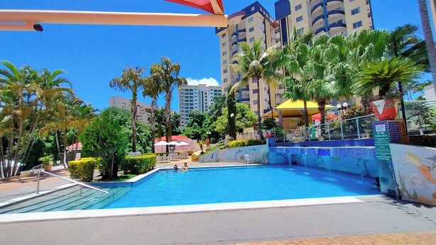 Una piscina con fuente, rodeada de palmeras y un edificio con balcones.
