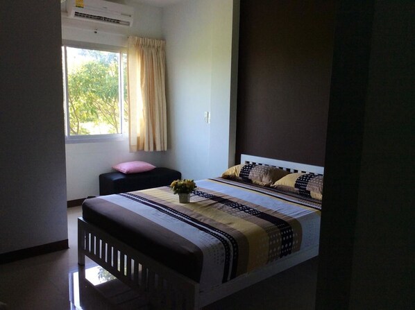 A bedroom with a bed, a bedside table, a window with curtains, and an air conditioning unit.