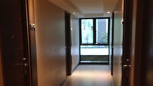 A corridor with doors on both sides, leading to a bright room with a view of buildings outside. - Big Zen Condotel (Nonthaburi)