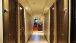 A hotel hallway with wooden doors, a tiled floor, and a staircase leading to an upper level. - Big Zen Condotel (Nonthaburi)