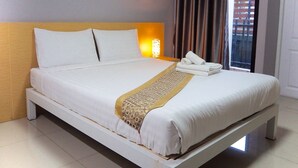 A neatly made bed with white linens and a decorative gold-patterned throw, a wooden headboard, and a wall-mounted picture of a coastal scene. - Big Zen Condotel (Nonthaburi)