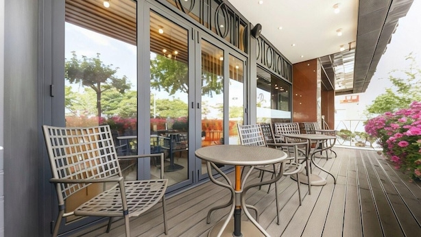 Une terrasse extérieure avec des chaises et des tables en métal, une entrée avec une porte vitrée et une vue sur la verdure.