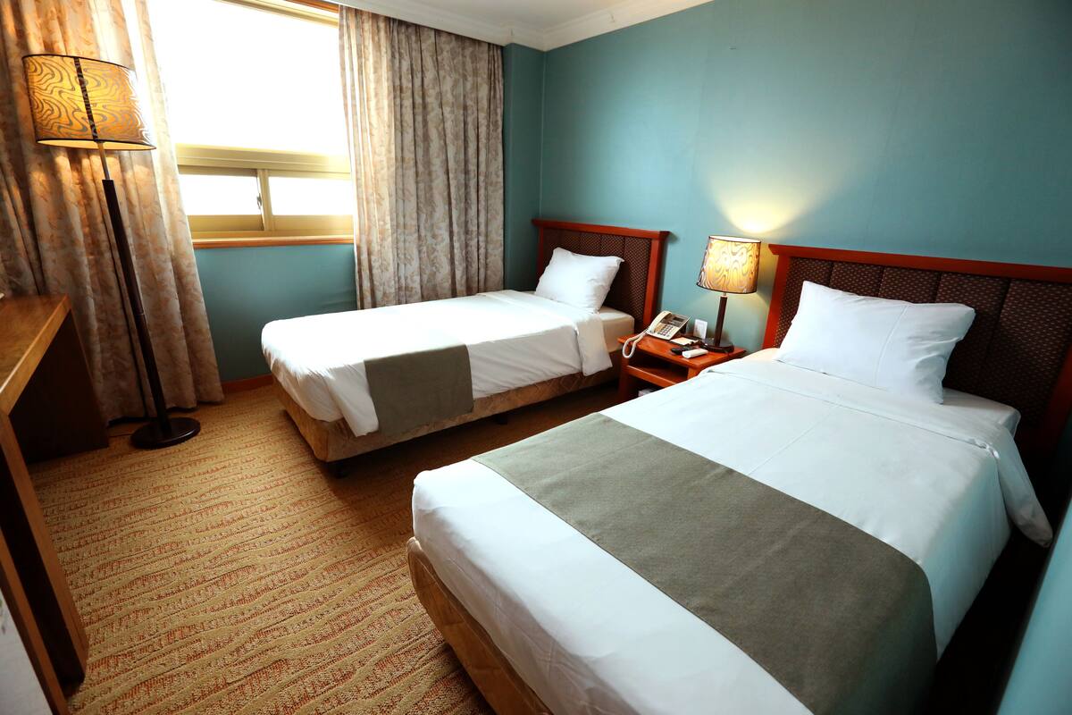 Una habitación de hotel con dos camas individuales, una mesita de noche con lámpara, teléfono y ventana con cortinas.
