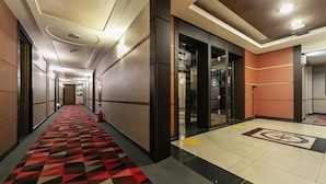 Un couloir d’hôtel avec un tapis à motifs, un éclairage encastré et un sol carrelé orné d’un logo.