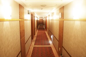 A hotel corridor with carpeted floors, wooden paneling, and wall-mounted light fixtures.