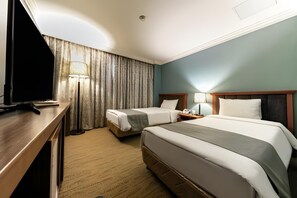 A hotel room with two beds, a desk, a TV, and a lamp.