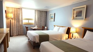 Une chambre d’hôtel avec deux lits, un bureau, une chaise, une table et une lampe.