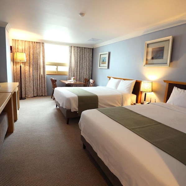 A hotel room with two beds, a desk, a chair, a table, and a lamp. - Prime Tourist Hotel (Busan)
