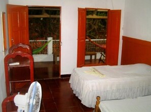 Una stanza con un letto, una sedia, un ventilatore e una finestra con porta aperta verso l'esterno.