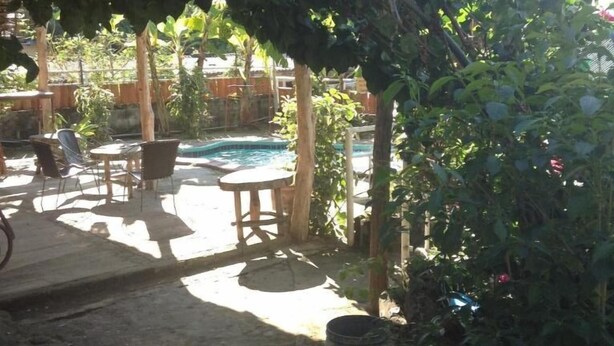 An outdoor patio area with a pool, wooden furniture, and lush greenery. - Hostel Tadeo San Juan del Sur (San Juan del Sur)