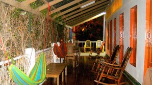 A covered outdoor seating area with wooden furniture, a hammock, and a railing. - Hostel Tadeo San Juan del Sur (San Juan del Sur)
