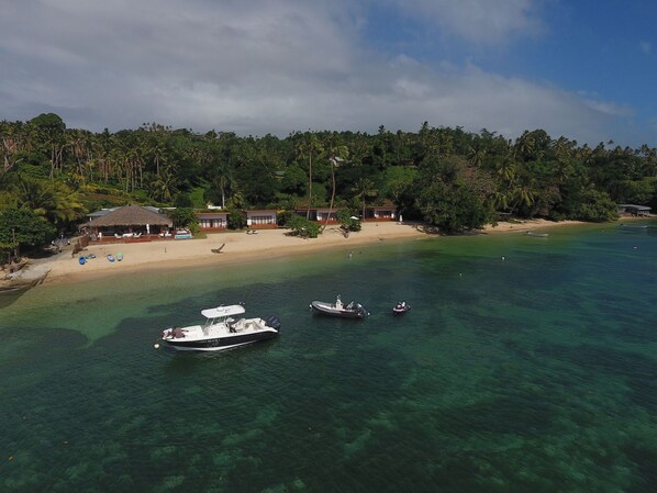 A beach resort with clear waters, boats, and a thatched-roof building. - Tides Reach Resort (Taveuni Island East)