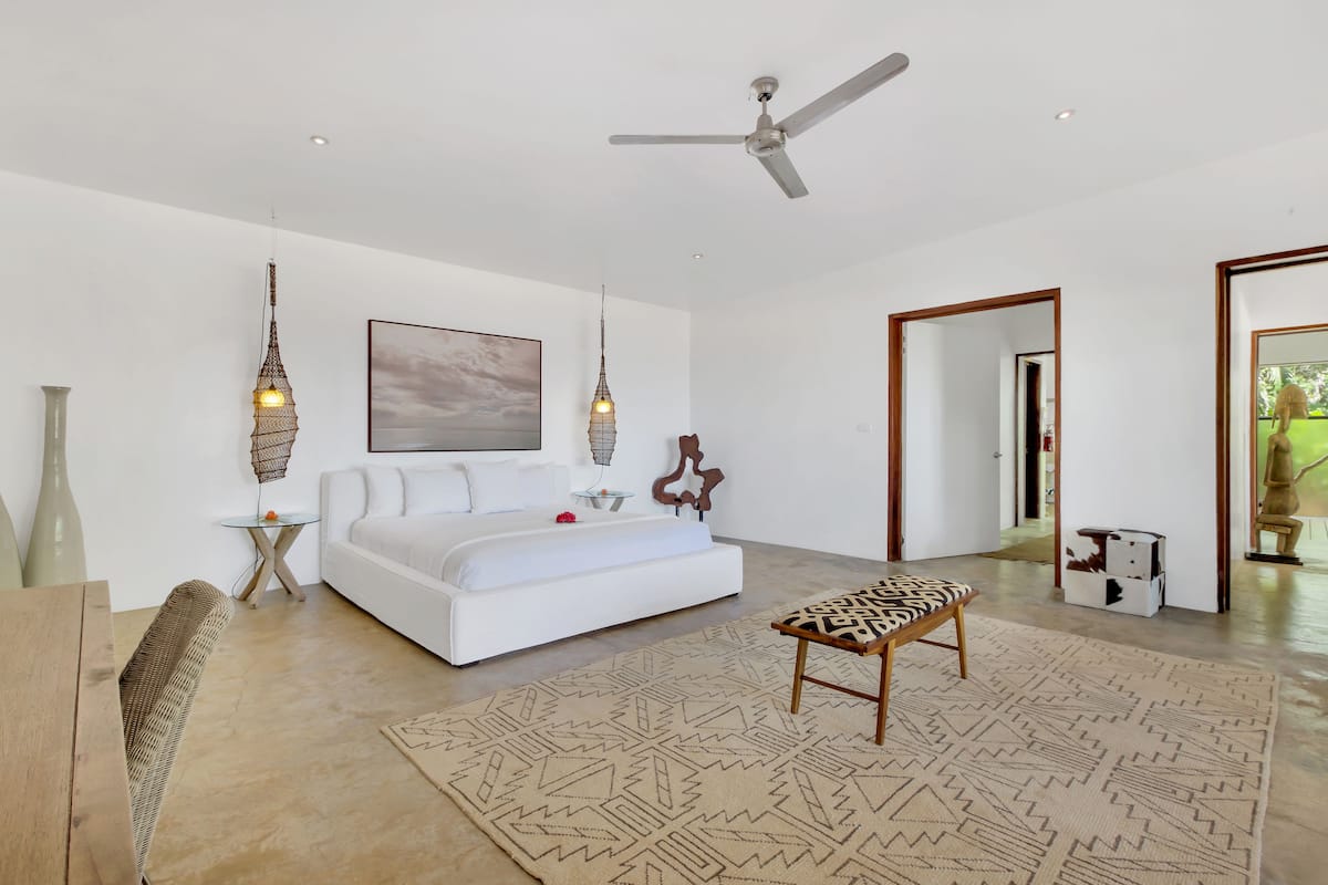 A modern bedroom with a white sofa, a patterned bench, and hanging lights.