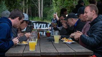 A group of people dining at a wooden picnic table outdoors.