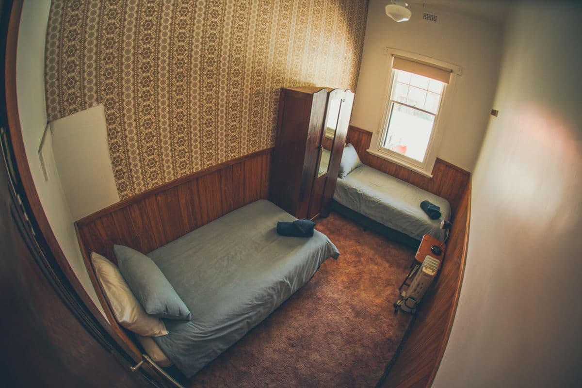 A room with two beds, a wardrobe, a window, and a carpeted floor.