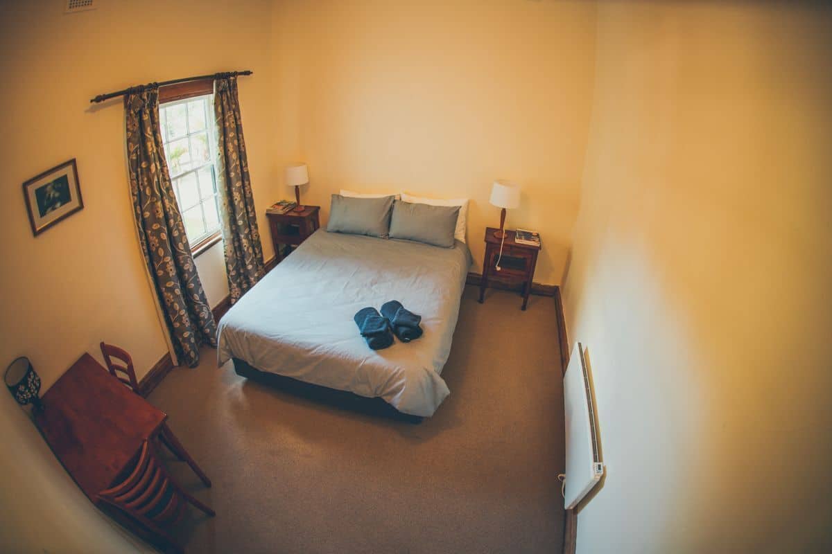 A bedroom with a bed, two bedside tables, a window with curtains, a chair, and a desk.