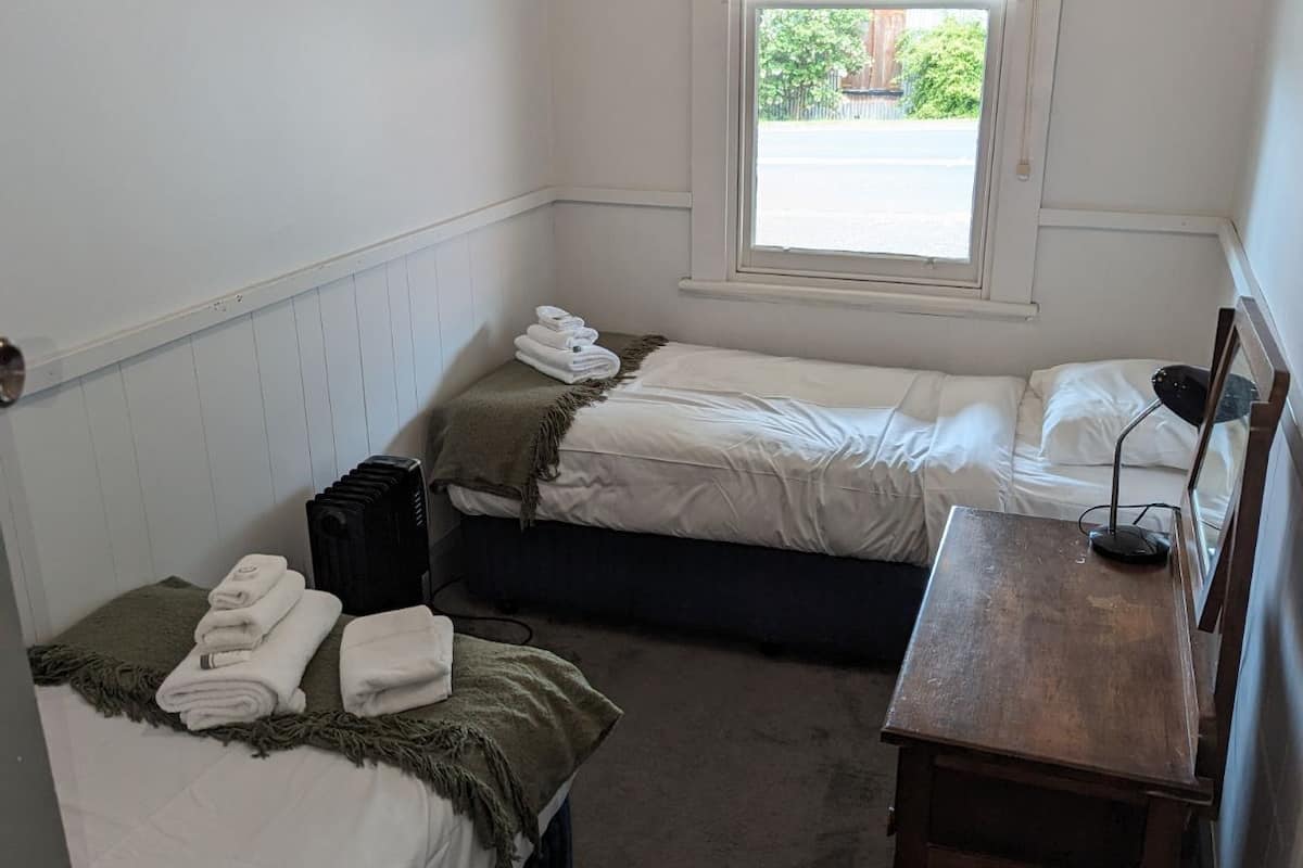 A small, simple room with two single beds, a small table, and a window.