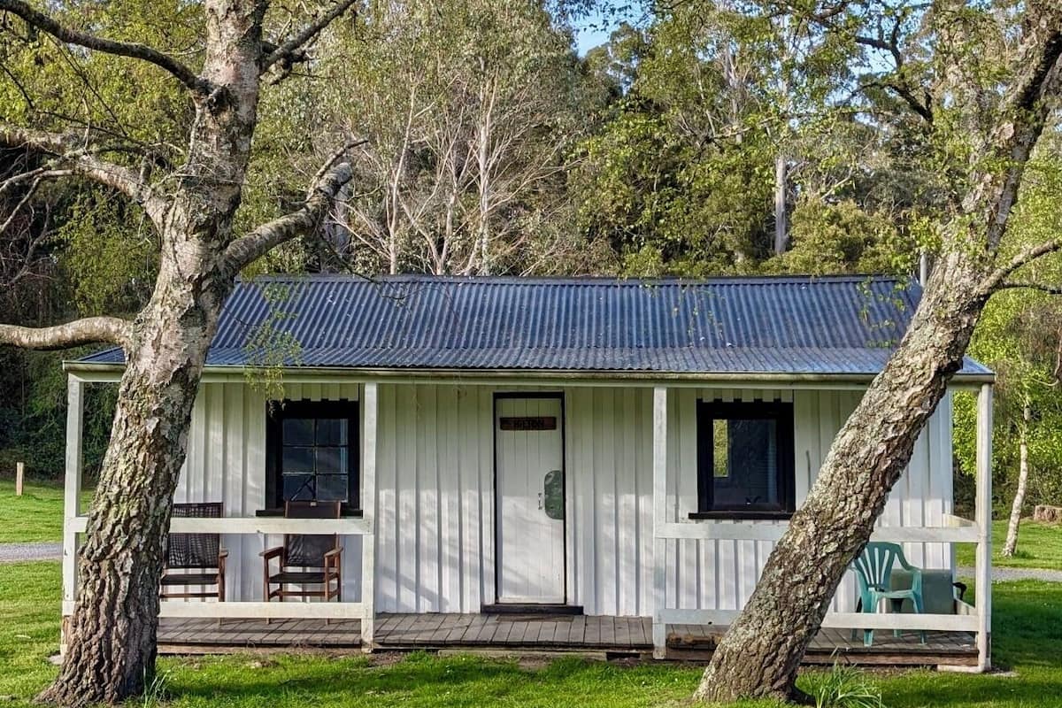 A small, single-story building with a corrugated metal roof, a front door, and a porch with chairs.
