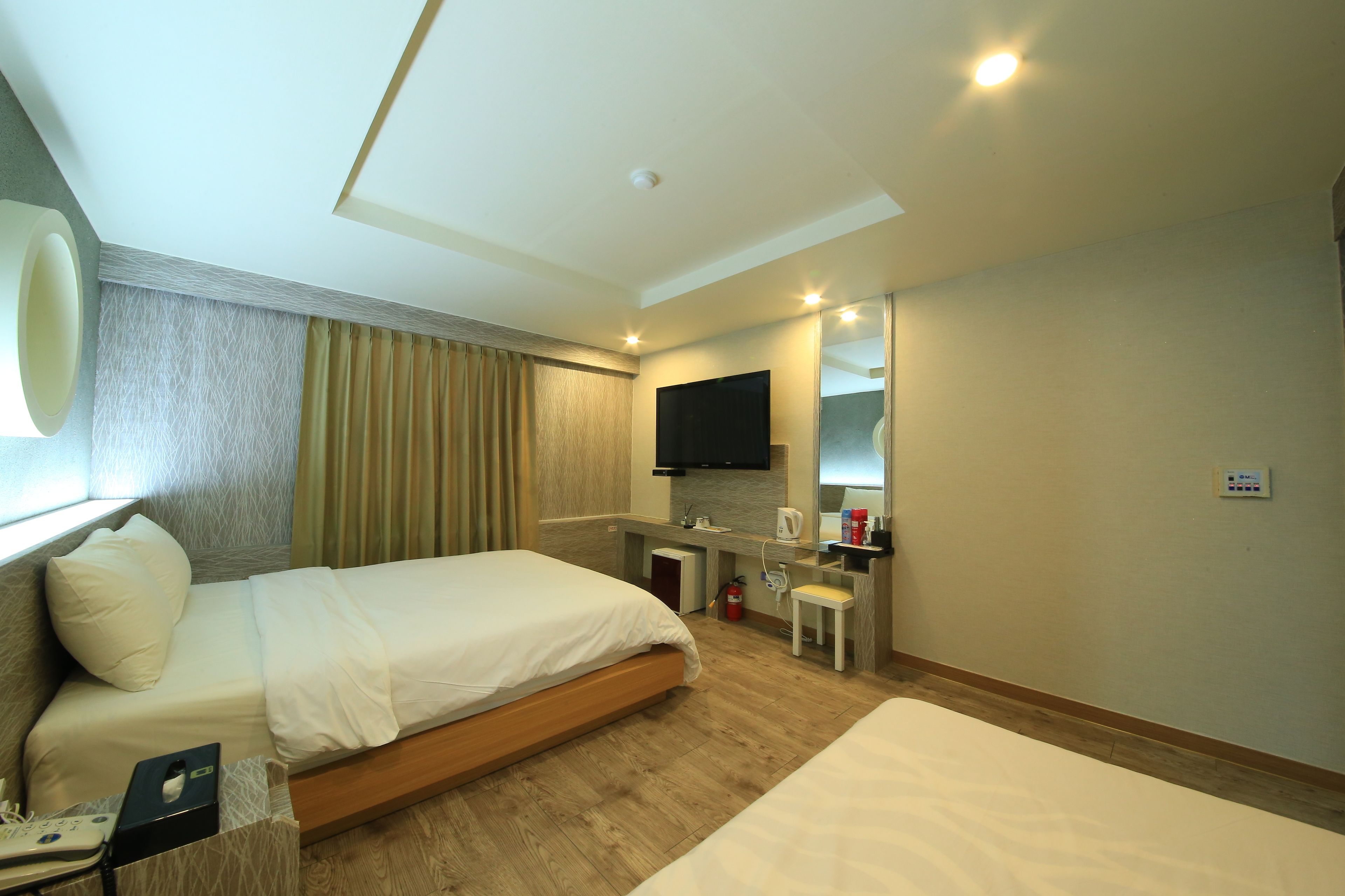 A hotel room with a large bed, a desk with a chair, a flat-screen TV, a mirror, and a small table with a telephone.